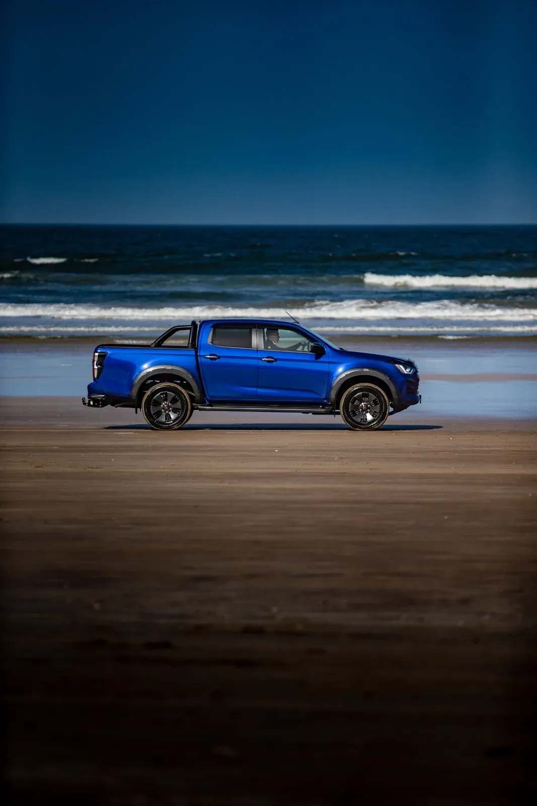 Blue pickup photographed on a wide sandy beach